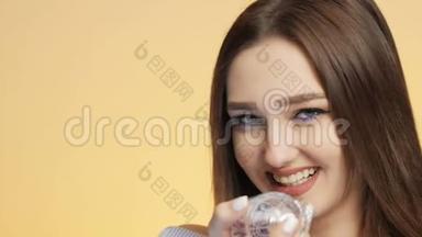 在<strong>彩色画</strong>室背景下美丽的女孩喜欢瓶子里的香水味，一个年轻的女人嗅着，笑着。